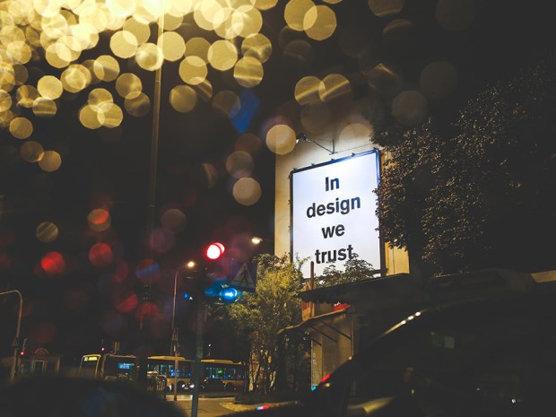A billboard with phrase In design we trust with lights and trees around 